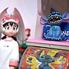 All three figures stand by a miniature Disney capsule machine which has a tiny Stitch from Lola and Stitch figure on top.
